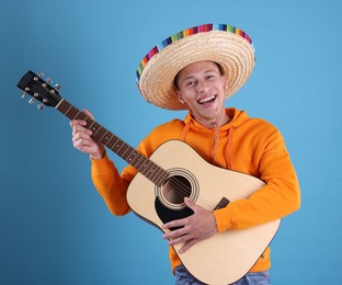 Photo of Happy man in sombrero hat playing guitar on light blue background