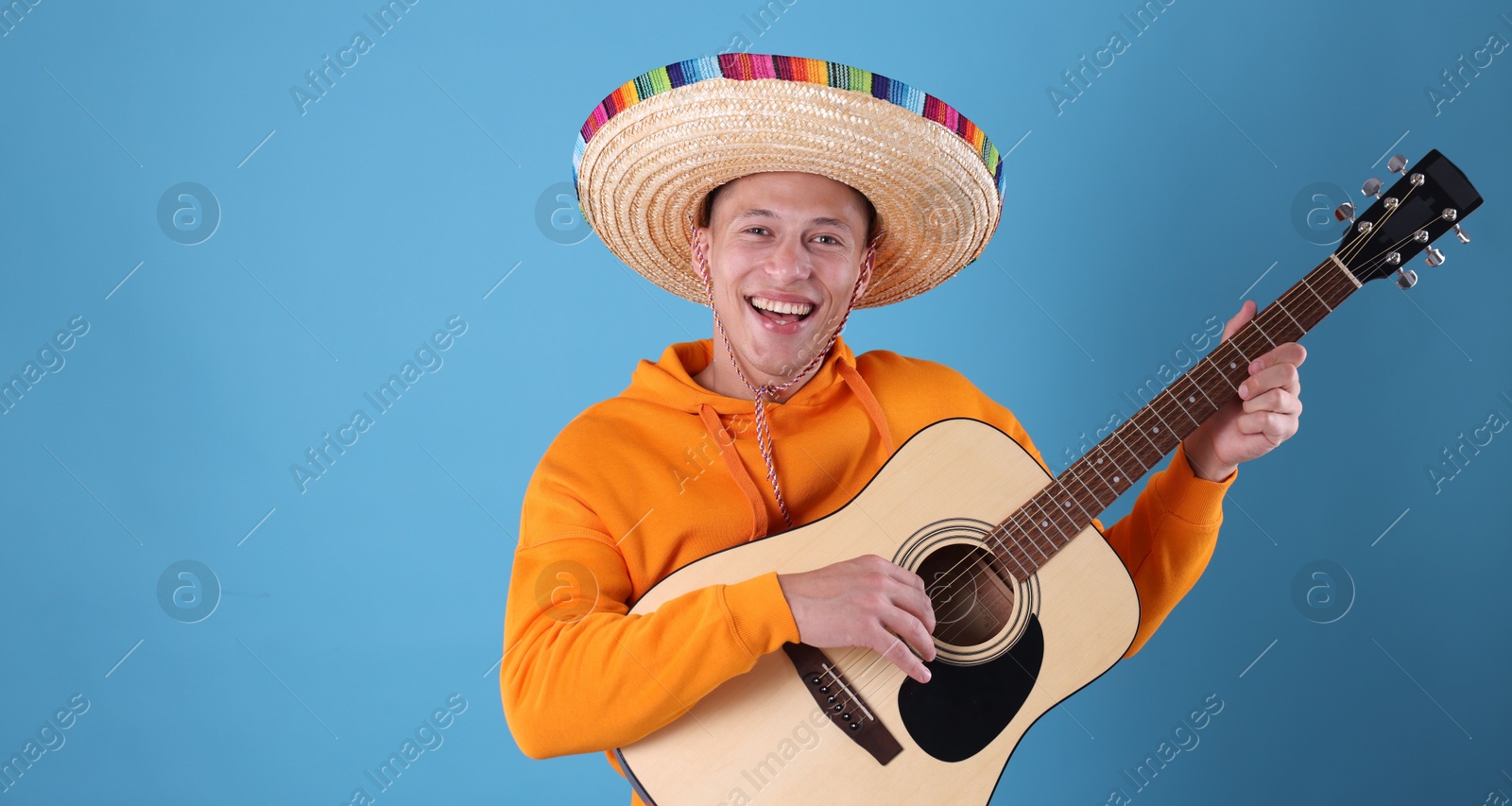 Photo of Happy man in sombrero hat playing guitar on light blue background
