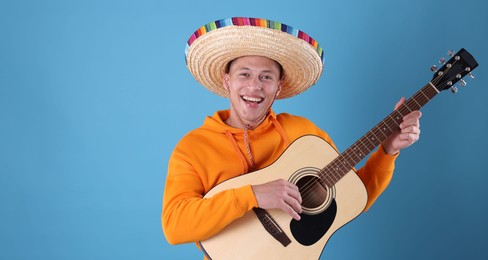Photo of Happy man in sombrero hat playing guitar on light blue background