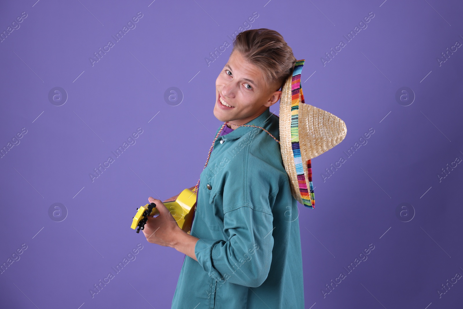 Photo of Happy man with sombrero hat playing ukulele on purple background