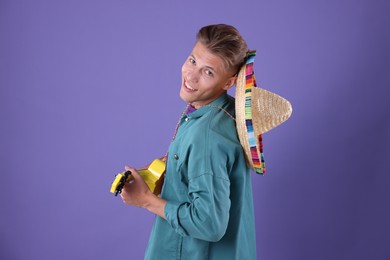 Photo of Happy man with sombrero hat playing ukulele on purple background
