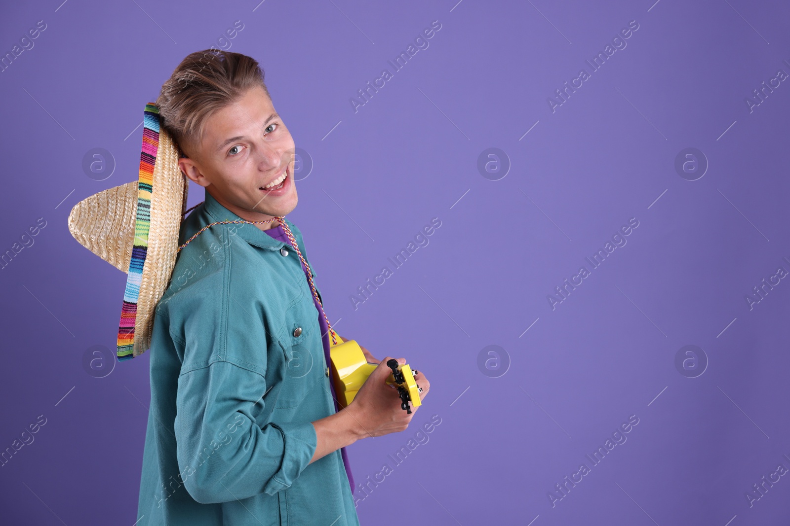 Photo of Happy man with sombrero hat playing ukulele on purple background. Space for text