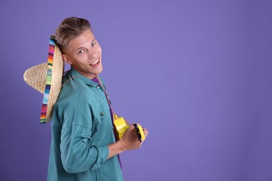 Photo of Happy man with sombrero hat playing ukulele on purple background. Space for text