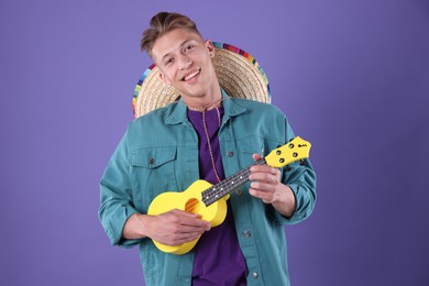 Photo of Happy man with sombrero hat playing ukulele on purple background