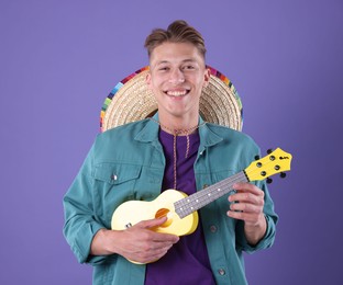 Photo of Happy man with sombrero hat playing ukulele on purple background