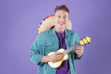 Photo of Happy man with sombrero hat playing ukulele on purple background