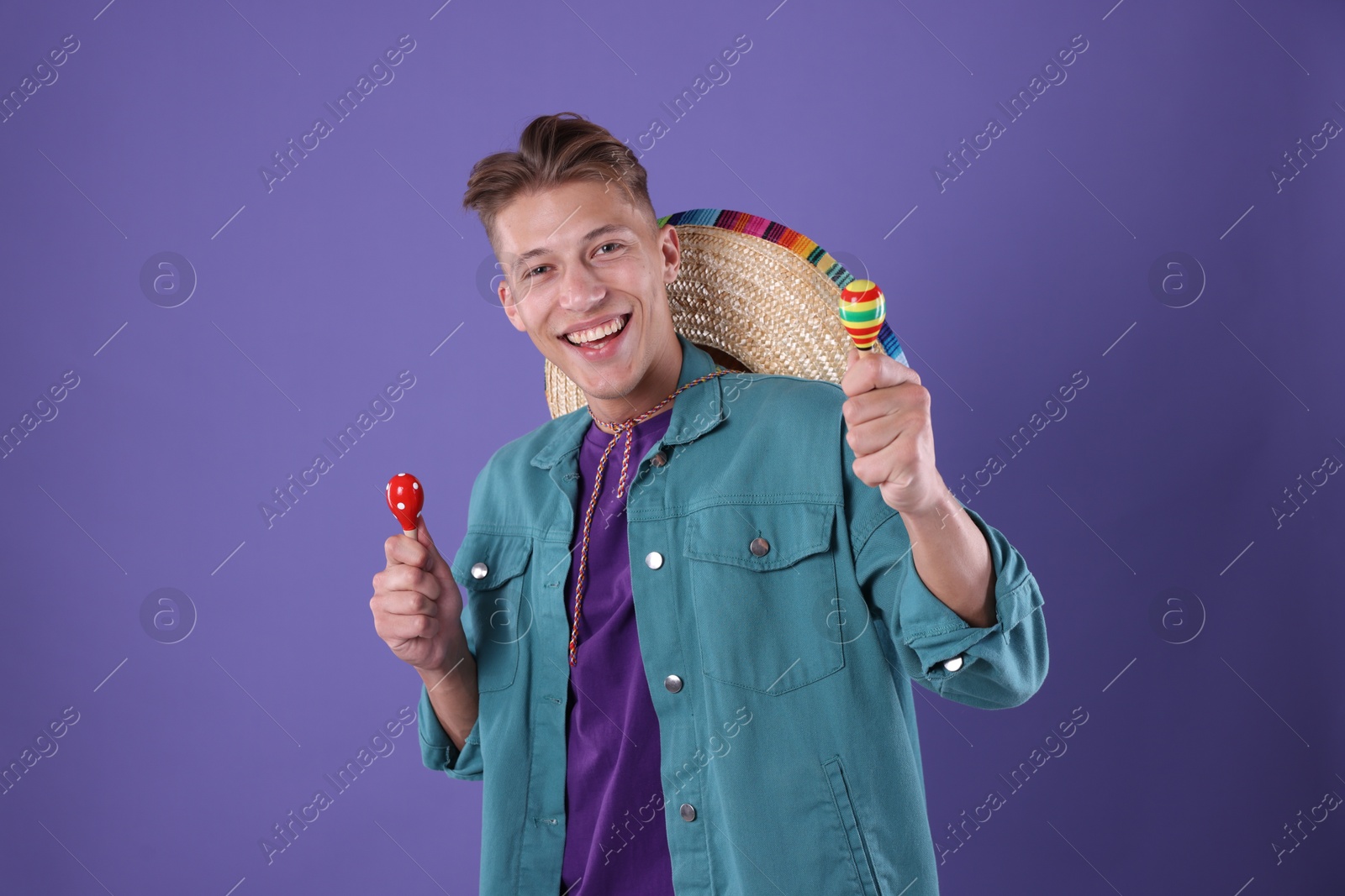 Photo of Happy man with sombrero hat playing maracas on purple background