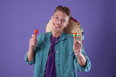 Photo of Happy man with sombrero hat playing maracas on purple background