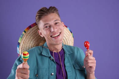 Photo of Happy man with sombrero hat playing maracas on purple background