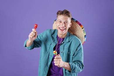 Photo of Happy man with sombrero hat playing maracas on purple background