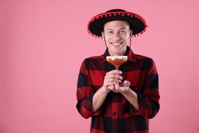 Photo of Smiling man in black Flamenco hat with cocktail on pink background. Space for text