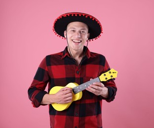 Photo of Smiling man in black Flamenco hat playing ukulele on pink background
