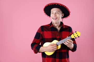 Photo of Smiling man in black Flamenco hat playing ukulele on pink background. Space for text