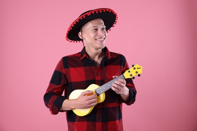 Photo of Smiling man in black Flamenco hat playing ukulele on pink background