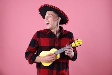 Photo of Smiling man in black Flamenco hat playing ukulele on pink background