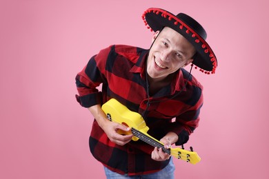 Photo of Smiling man in black Flamenco hat playing ukulele on pink background