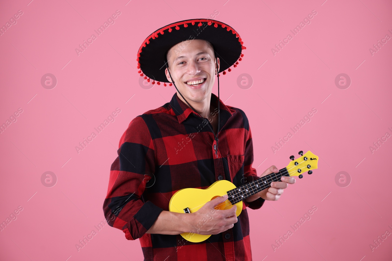 Photo of Smiling man in black Flamenco hat playing ukulele on pink background