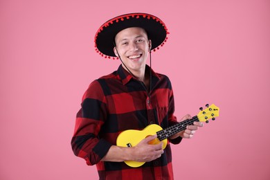 Photo of Smiling man in black Flamenco hat playing ukulele on pink background