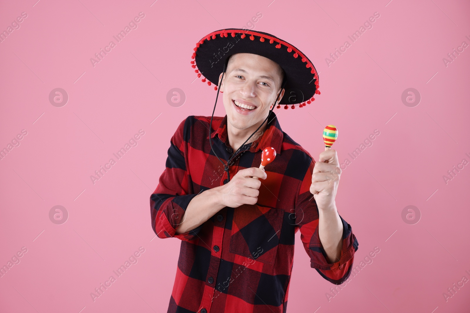Photo of Smiling man in black Flamenco hat playing maracas on pink background