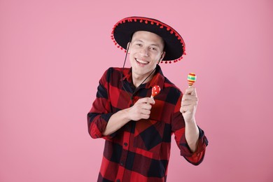 Photo of Smiling man in black Flamenco hat playing maracas on pink background