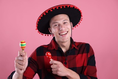 Photo of Smiling man in black Flamenco hat playing maracas on pink background