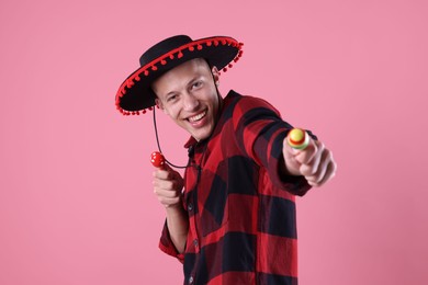 Photo of Smiling man in black Flamenco hat playing maracas on pink background