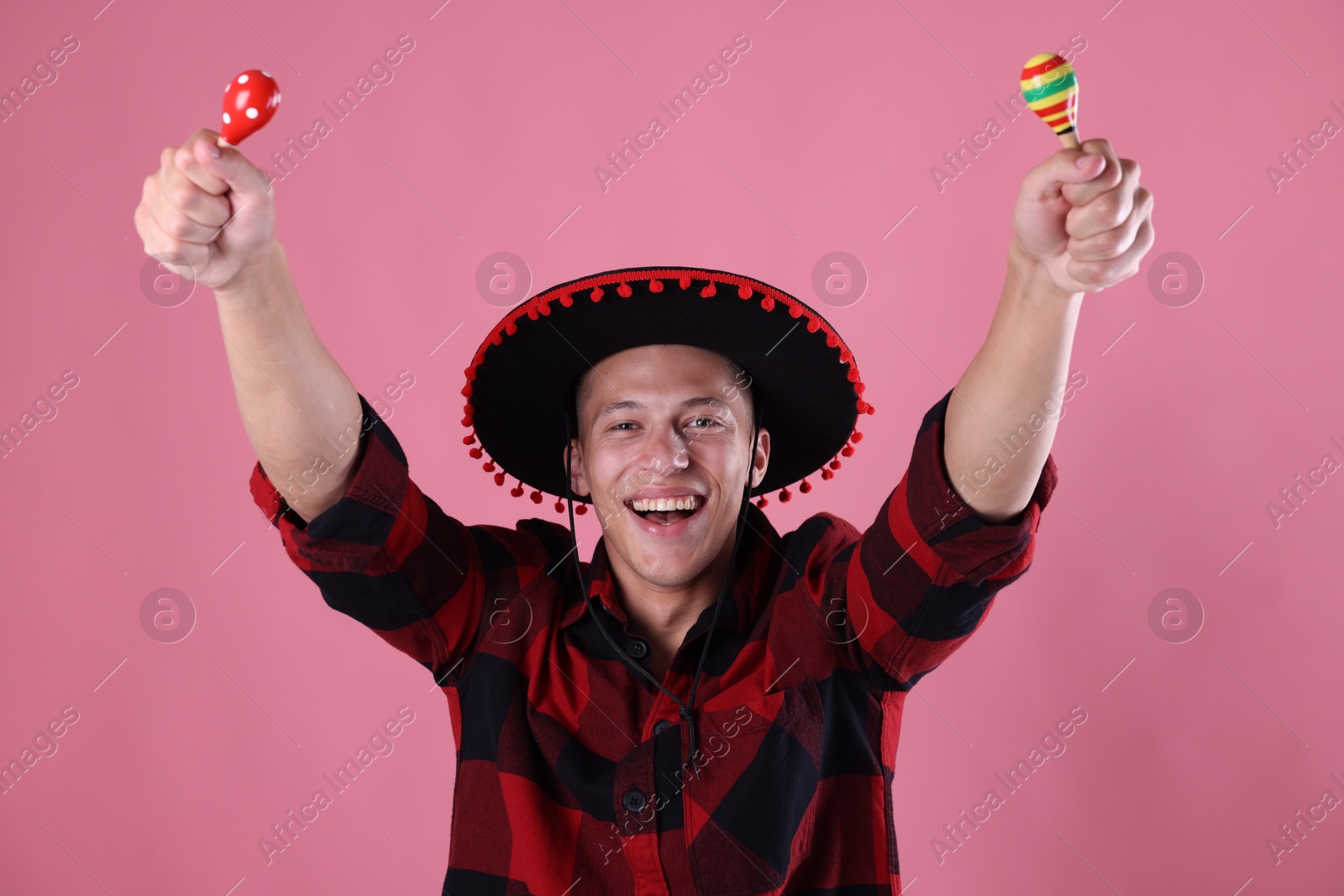 Photo of Smiling man in black Flamenco hat playing maracas on pink background
