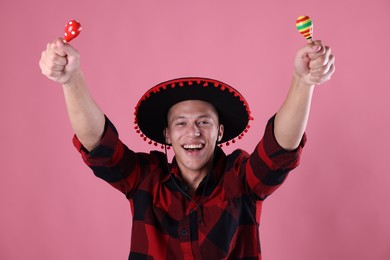 Photo of Smiling man in black Flamenco hat playing maracas on pink background