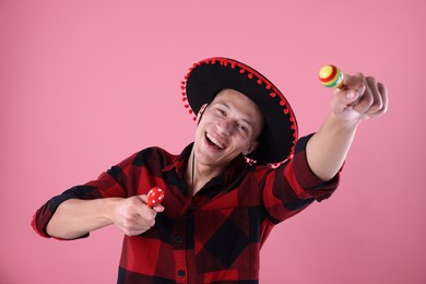 Photo of Smiling man in black Flamenco hat playing maracas on pink background