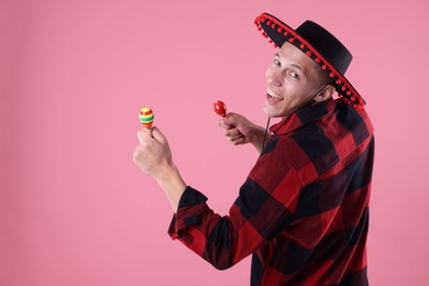 Photo of Smiling man in black Flamenco hat playing maracas on pink background