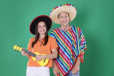 Photo of Happy couple in sombrero and Flamenco hats playing musical instruments on green background