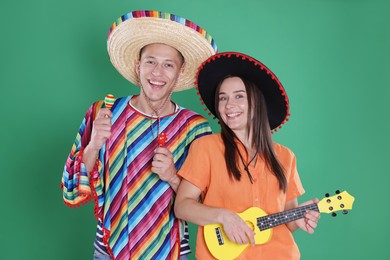 Photo of Happy couple in sombrero and Flamenco hats playing musical instruments on green background