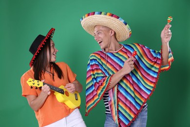 Photo of Happy couple in sombrero and Flamenco hats playing musical instruments on green background