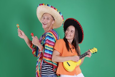 Photo of Happy couple in sombrero and Flamenco hats playing musical instruments on green background