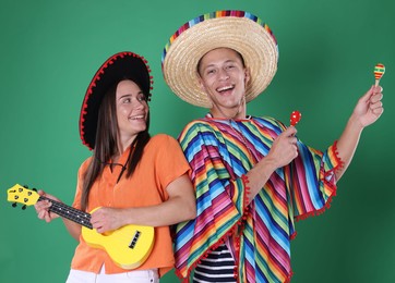Photo of Happy couple in sombrero and Flamenco hats playing musical instruments on green background