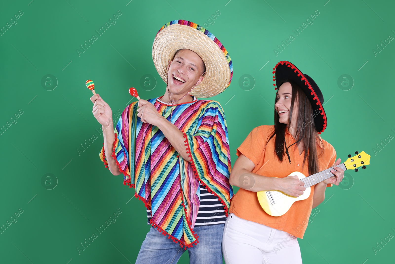 Photo of Happy couple in sombrero and Flamenco hats playing musical instruments on green background