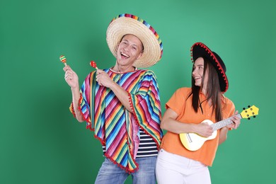 Photo of Happy couple in sombrero and Flamenco hats playing musical instruments on green background
