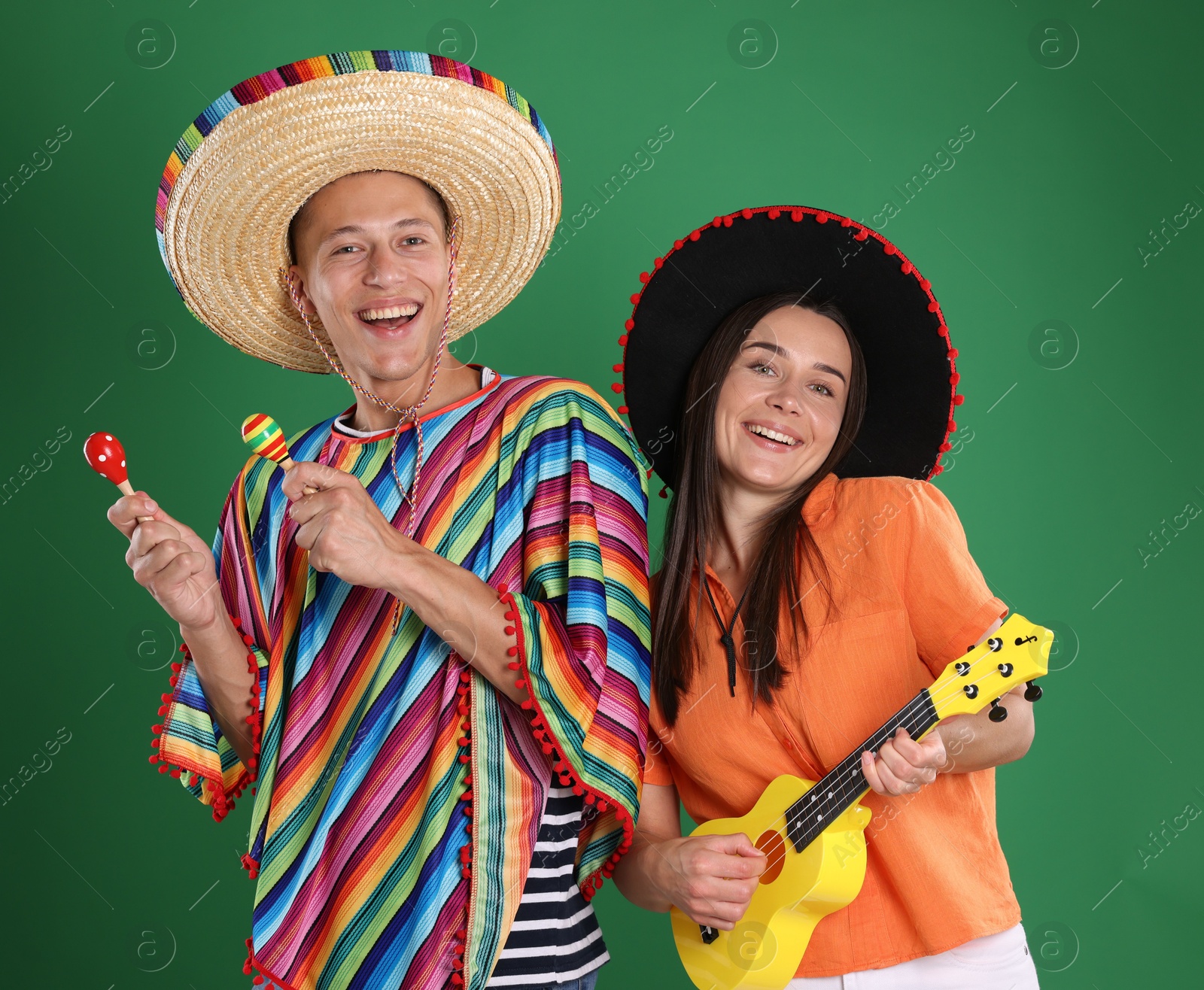 Photo of Happy couple in sombrero and Flamenco hats playing musical instruments on green background
