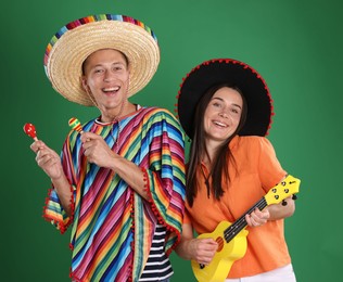 Photo of Happy couple in sombrero and Flamenco hats playing musical instruments on green background