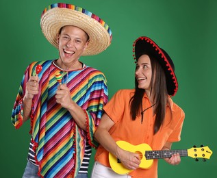 Photo of Happy couple in sombrero and Flamenco hats playing musical instruments on green background