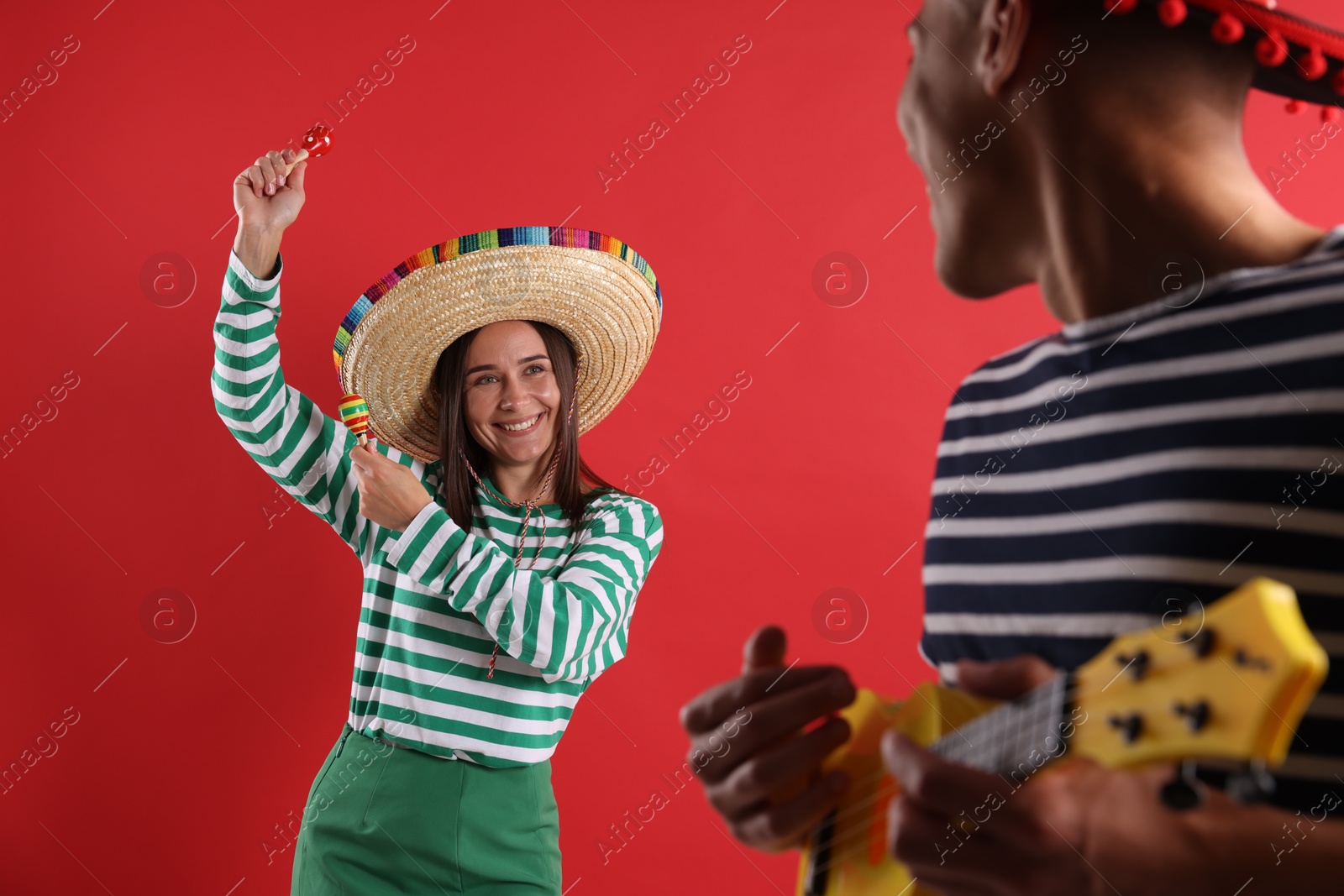 Photo of Happy couple in sombrero and Flamenco hats playing musical instruments on red background
