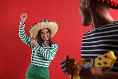 Photo of Happy couple in sombrero and Flamenco hats playing musical instruments on red background