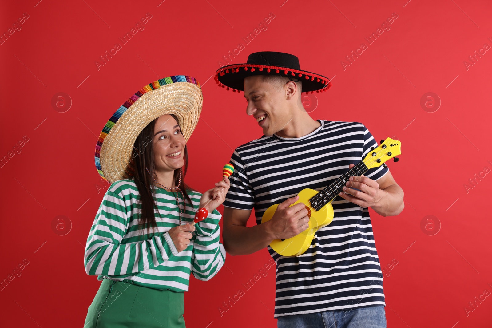 Photo of Happy couple in sombrero and Flamenco hats playing musical instruments on red background