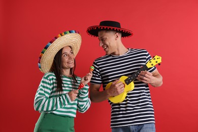 Photo of Happy couple in sombrero and Flamenco hats playing musical instruments on red background