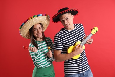 Photo of Happy couple in sombrero and Flamenco hats playing musical instruments on red background