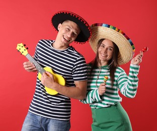 Photo of Happy couple in sombrero and Flamenco hats playing musical instruments on red background