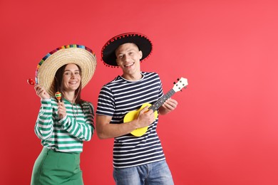 Photo of Happy couple in sombrero and Flamenco hats playing musical instruments on red background