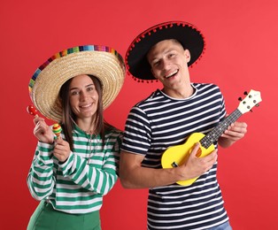 Photo of Happy couple in sombrero and Flamenco hats playing musical instruments on red background