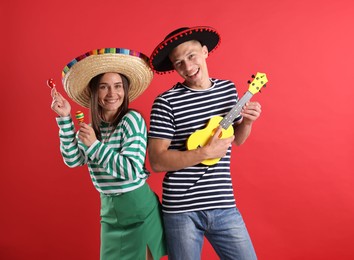 Photo of Happy couple in sombrero and Flamenco hats playing musical instruments on red background