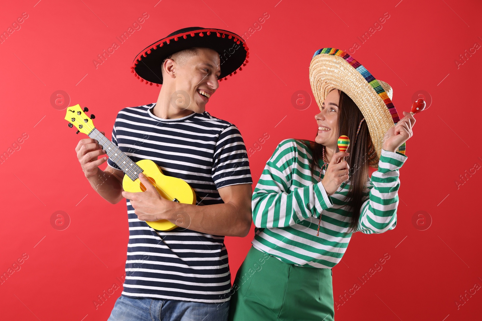 Photo of Happy couple in sombrero and Flamenco hats playing musical instruments on red background
